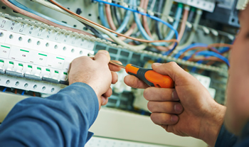 Electrical contractor working in fuse box. Elite Electrical saves hours tracking employee time and running payroll